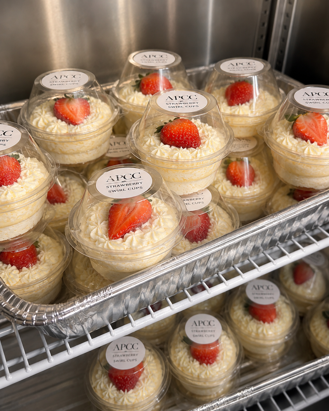 Tray of APCC strawberry swirl cup cheesecakes on metal cooling racks — banquet-ready packaging